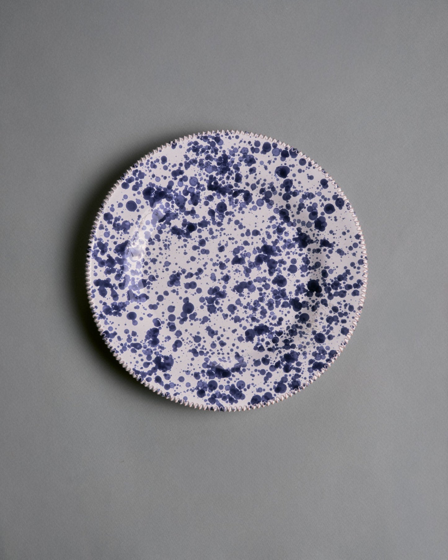 Assiette artisanale en céramique émaillée, réalisées par la manufacture Suma Ceramiche Artistiche dans la région des Pouilles, Italie. Pièce arborant un décor moucheté bleu profond sur fond blanc appliqué à la main. Parfait état.