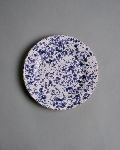 Assiette artisanale en céramique émaillée, réalisées par la manufacture Suma Ceramiche Artistiche dans la région des Pouilles, Italie. Pièce arborant un décor moucheté bleu profond sur fond blanc appliqué à la main. Parfait état.