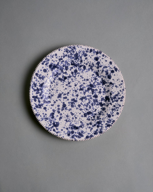 Assiette artisanale en céramique émaillée, réalisées par la manufacture Suma Ceramiche Artistiche dans la région des Pouilles, Italie. Pièce arborant un décor moucheté bleu profond sur fond blanc appliqué à la main. Parfait état.