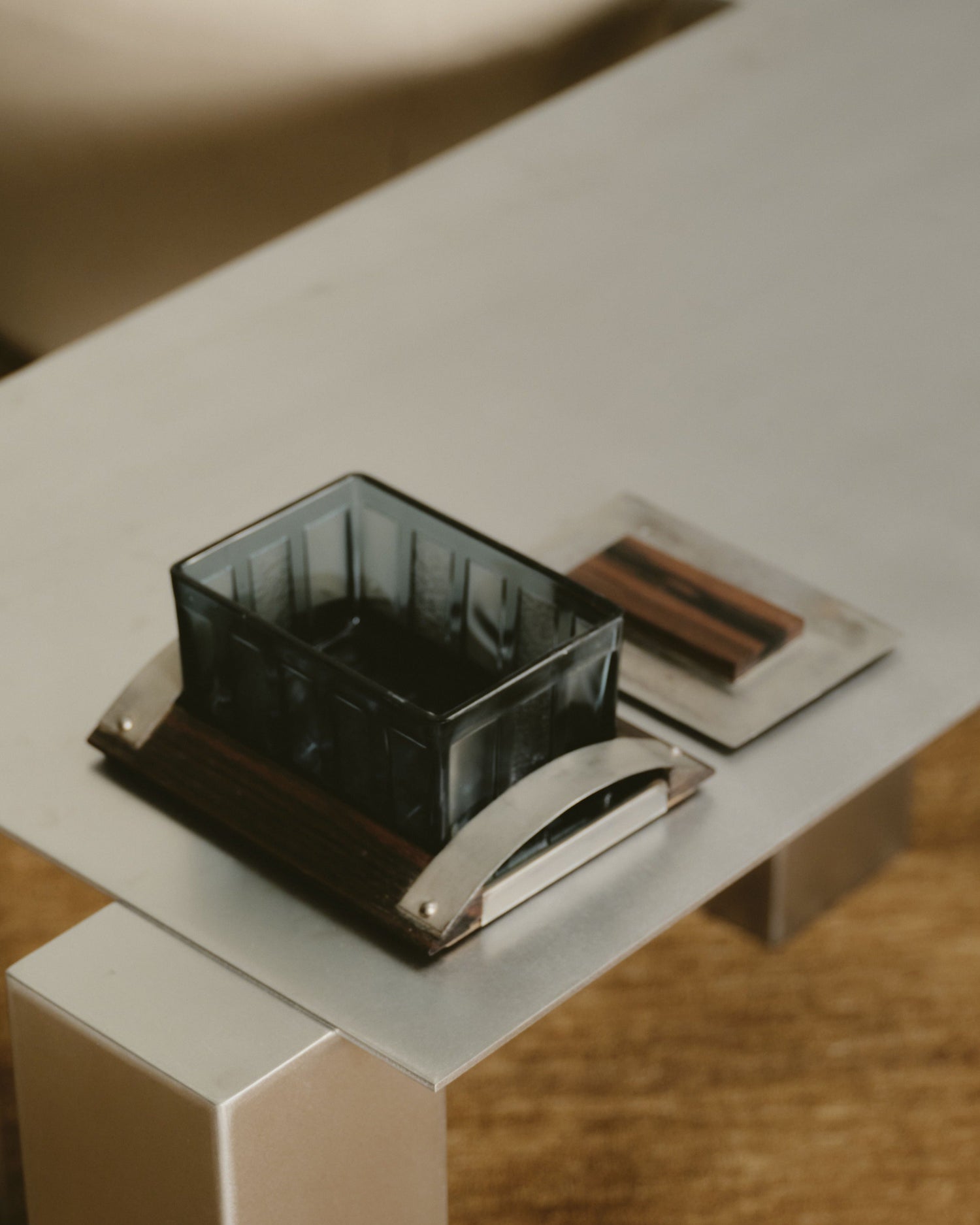 Boîte de style Art Déco en métal et en verre bleu à pans alternés lisses et rugueux. Plateau en bois recouvert d'un miroir, à bordure et couvercle en bois et métal. Travail des années 1970. Bel état général, à noter une légère patine conforme à l'âge et à l'usage.