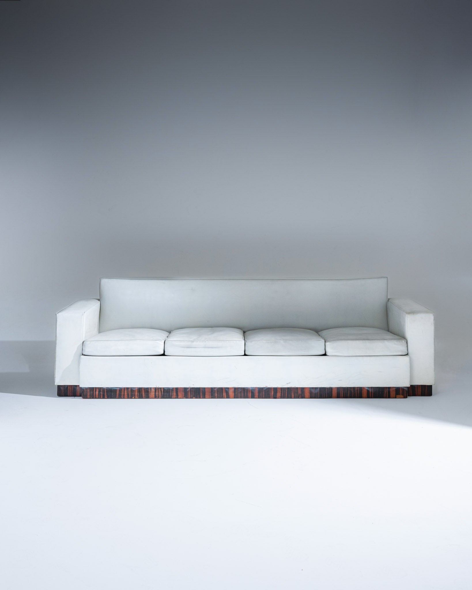 Canapé quatre places de Jacques Adnet (1900-1984), réalisé dans les années 1930. Modèle rectiligne revêtu d’un cuir gris clair, reposant sur un élégant socle en placage de palissandre. Assise profonde composée de coussins amovibles en cuir.
Très bel état général, présentant une patine naturelle et quelques traces d’usage conformes à l’âge et à l'usage.