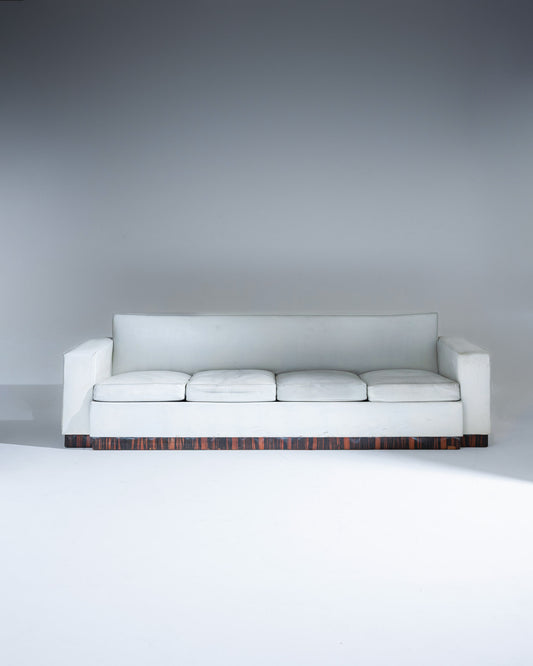 Canapé quatre places de Jacques Adnet (1900-1984), réalisé dans les années 1930. Modèle rectiligne revêtu d’un cuir gris clair, reposant sur un élégant socle en placage de palissandre. Assise profonde composée de coussins amovibles en cuir.
Très bel état général, présentant une patine naturelle et quelques traces d’usage conformes à l’âge et à l'usage.