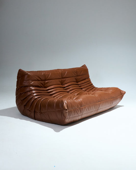 Canapé trois places TOGO du designer Michel Ducaroy (1925-2009) pour Ligne Roset dans les années 1970. Grand classique du design cette chauffeuse entièrement en mousse est recouverte d'une housse en cuir brun d'origine. Pièce étiqueté.
Très bon état général. À noter, une légère décoloration du cuir à certains endroits (voir photo).