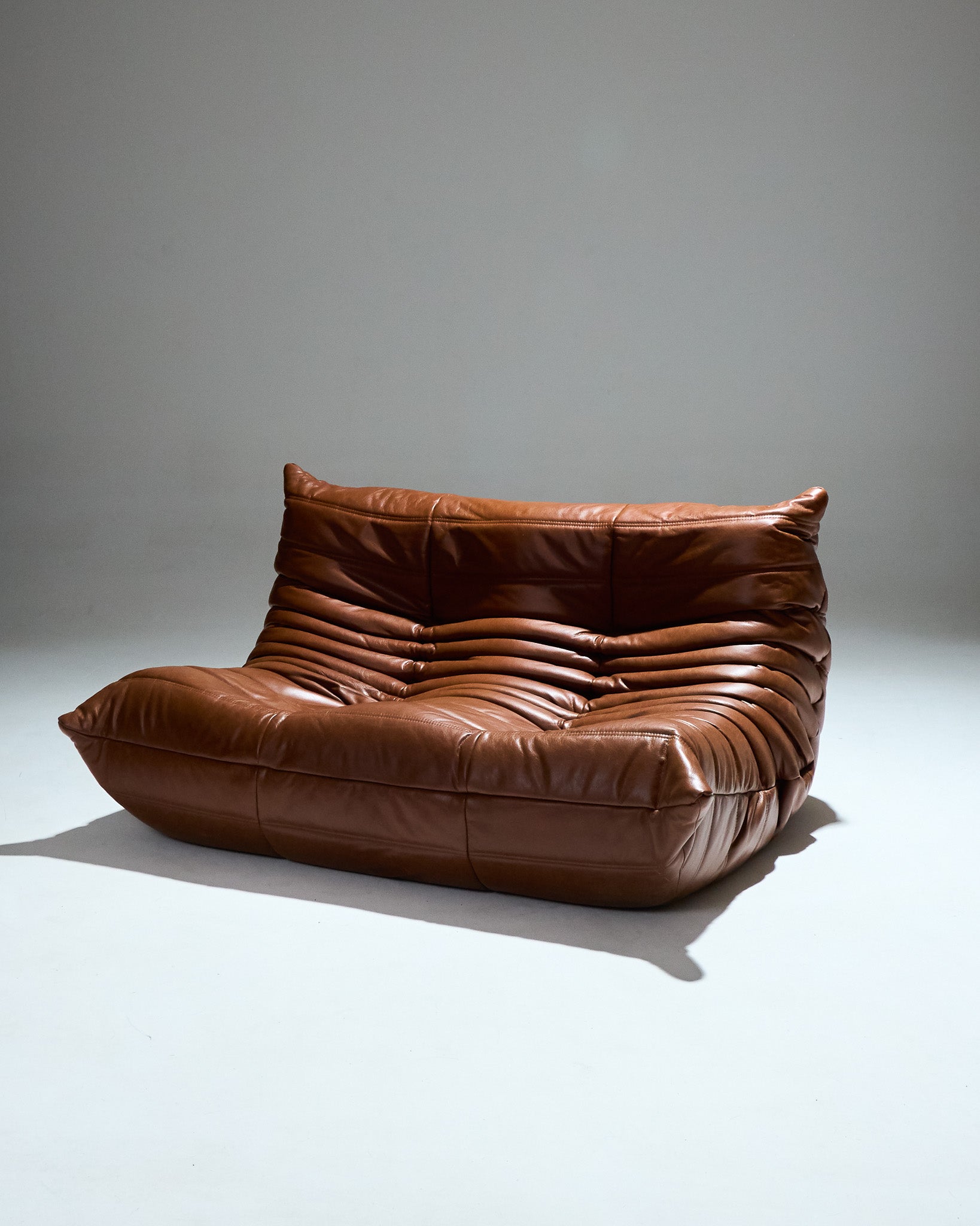 Canapé deux places TOGO du designer Michel Ducaroy (1925-2009) pour Ligne Roset dans les années 1970. Grand classique du design cette chauffeuse entièrement en mousse est recouverte d'une housse en cuir brun d'origine. Pièce étiqueté.
Très bon état général. À noter légère décoloration du cuir à certains endroits (voir photo).