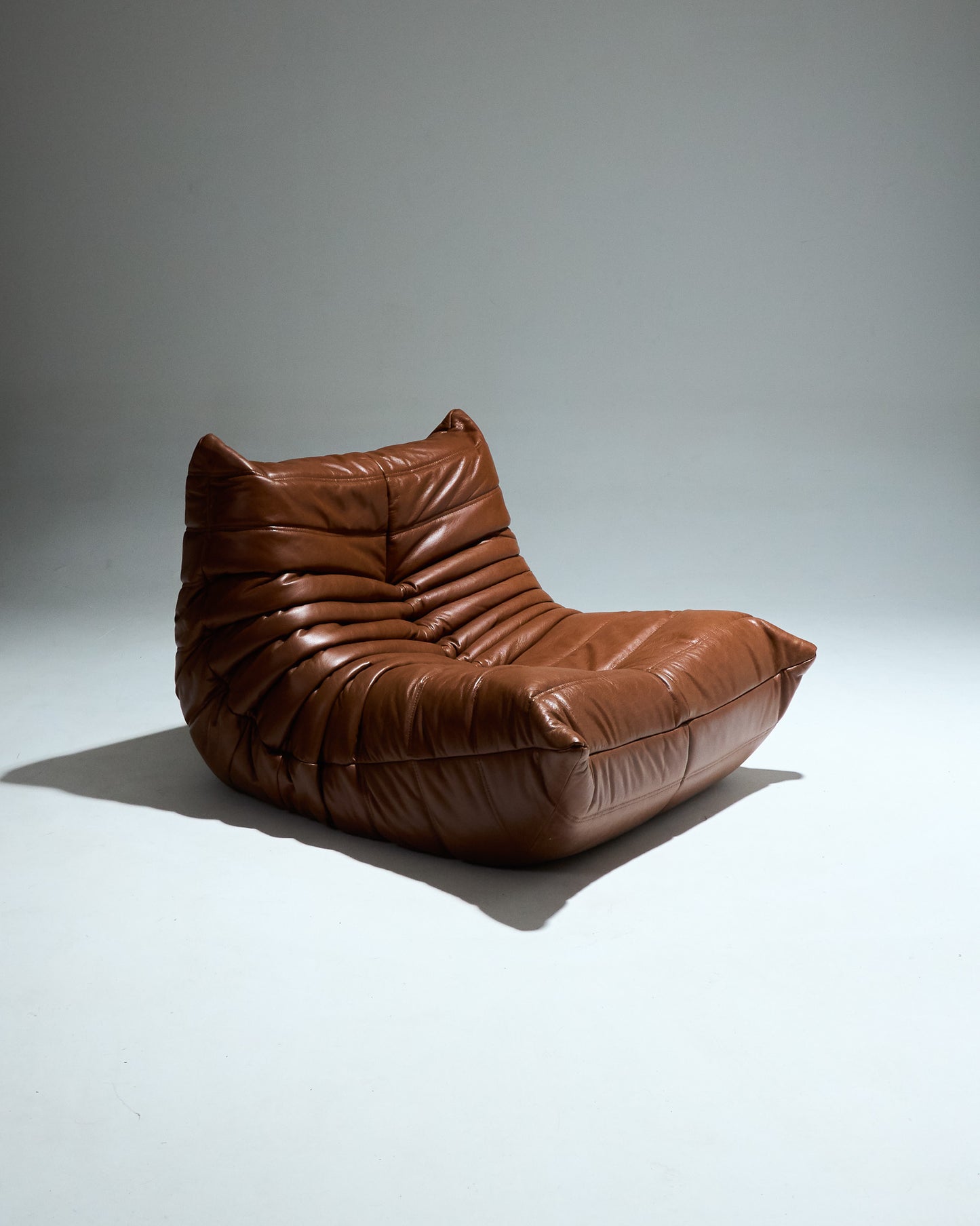 Fauteuil TOGO du designer Michel Ducaroy (1925-2009) pour Ligne Roset dans les années 1970. Grand classique du design cette chauffeuse entièrement en mousse est recouverte d'une housse en cuir brun d'origine. Pièce étiqueté.
Très bon état général. À noter légère décoloration du cuir à certains endroits (voir photo).