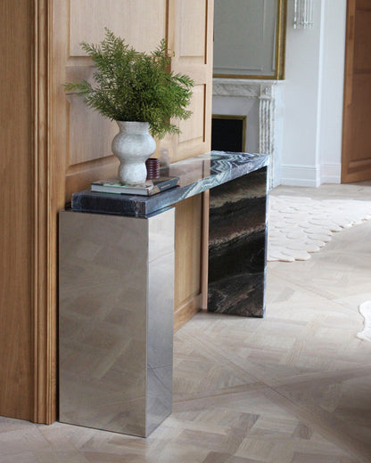 Console modèle "Jill" en marbre cipolin et inox, par Marbera. La console Jill allie élégance et modernité grâce à son design asymétrique qui mêle un cube rectangulaire en inox à un plateau et un piétement en marbre&nbsp; veiné.