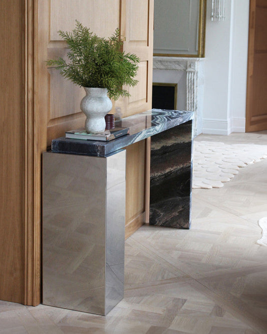 Console modèle "Jill" en marbre cipolin et inox, par Marbera. La console Jill allie élégance et modernité grâce à son design asymétrique qui mêle un cube rectangulaire en inox à un plateau et un piétement en marbre&nbsp; veiné.