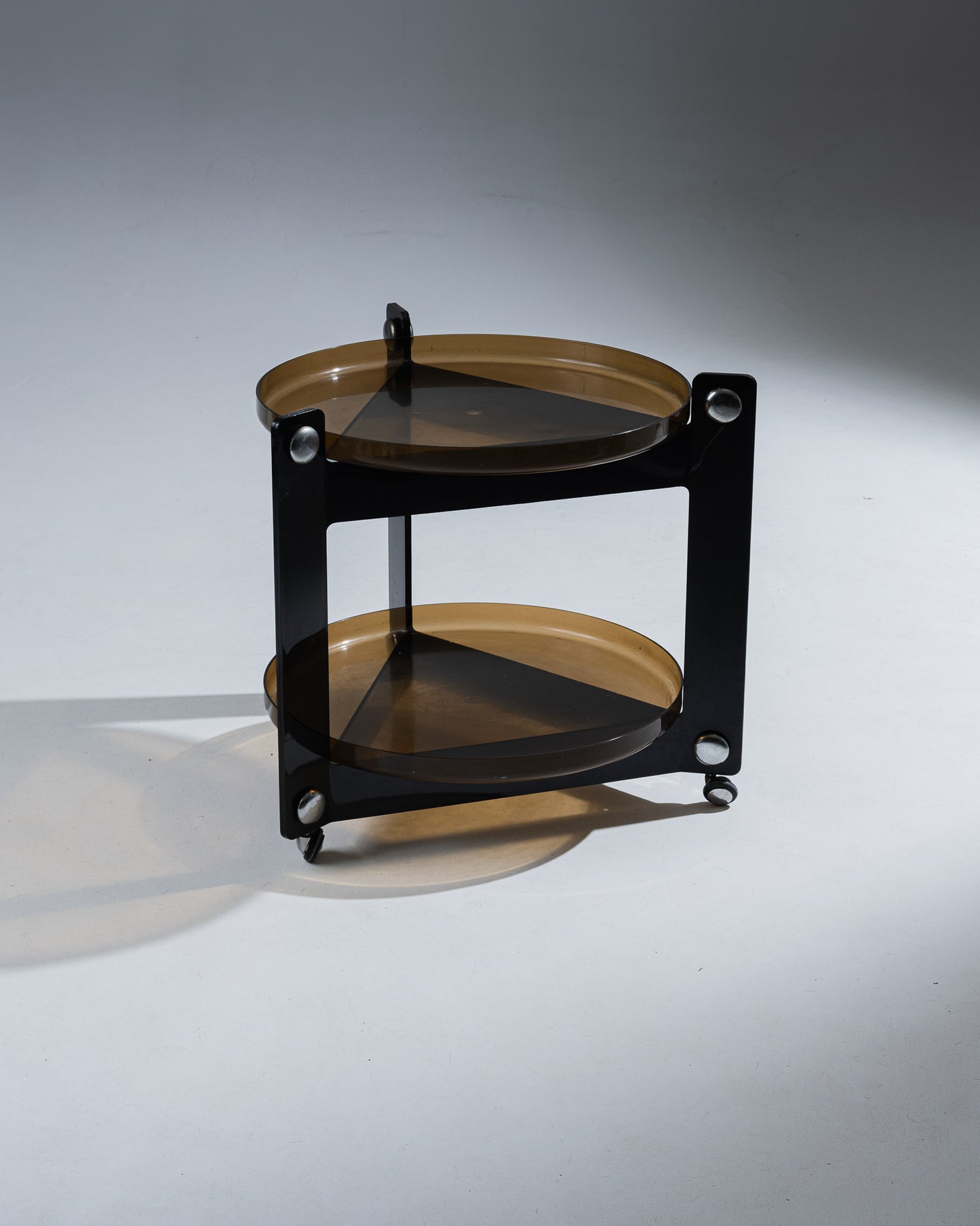 Desserte à deux plateaux amovibles en plexiglass fumé et roulettes. Conçu par Luigi Massoni et produit par Guzzini dans les années 1970. Les formes de ce meuble opposent les triangles du corps aux plateaux ronds. Présente une rayure sur un des pieds, non visible une fois les plateaux posés. Non signée.&nbsp;
Marques conformes à l'âge et à l'usage.&nbsp;