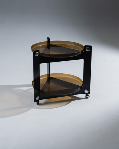 Desserte à deux plateaux amovibles en plexiglass fumé et roulettes. Conçu par Luigi Massoni et produit par Guzzini dans les années 1970. Les formes de ce meuble opposent les triangles du corps aux plateaux ronds. Présente une rayure sur un des pieds, non visible une fois les plateaux posés. Non signée.&nbsp;
Marques conformes à l'âge et à l'usage.&nbsp;
