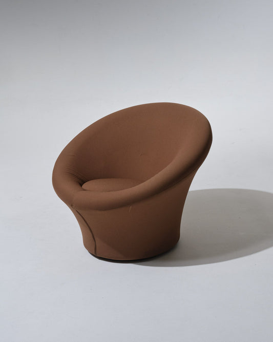 Fauteuil Mushroom de Pierre Paulin, années 1970. Dans une esthétique typique du Space Age, il se compose d'une coque en fibre de verre, garni de son tissu d’origine marron. Le pied circulaire évasé forme d’un seul tenant l’assise et le dossier, également circulaires. Le tissu présente une usure marquée, cohérente avec l’âge.