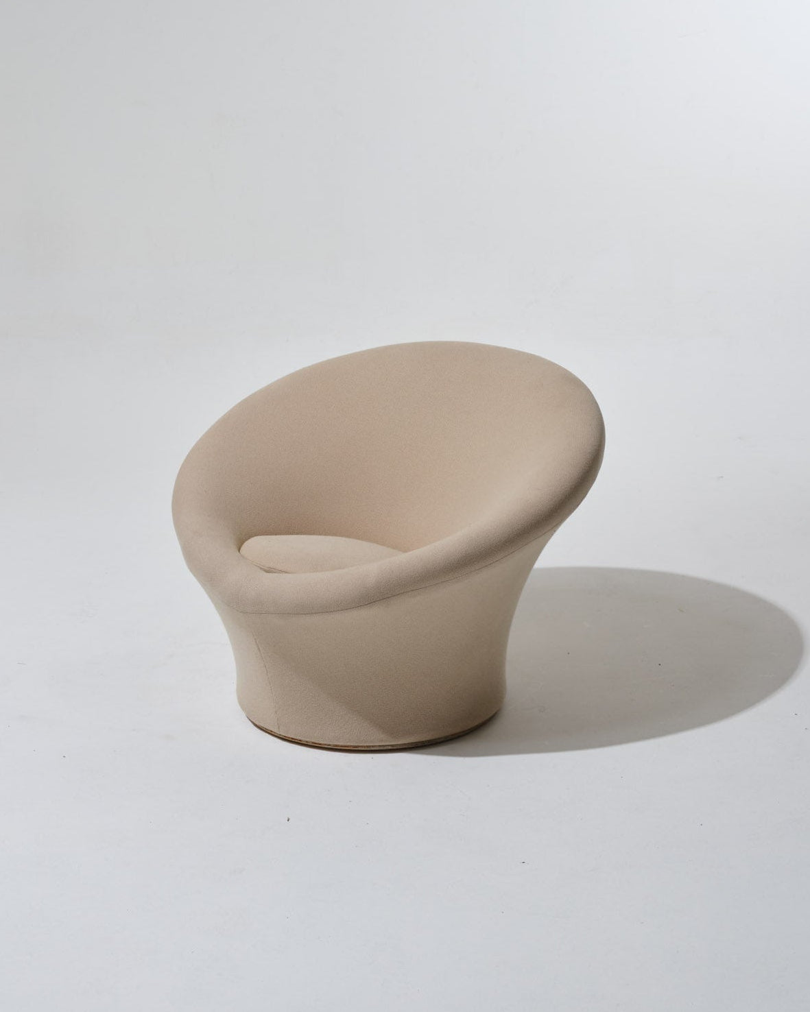 Fauteuil Mushroom de Pierre Paulin, années 1970. Dans une esthétique typique du Space Age, il se compose d'une coque en fibre de verre, garni de son tissu Kvadrat beige. Le pied circulaire évasé forme d’un seul tenant l’assise et le dossier, également circulaires. Le tissu présente une usure cohérente avec l’âge et l’usage.