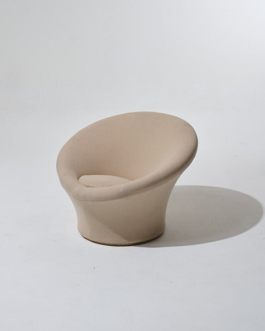 Fauteuil Mushroom de Pierre Paulin, années 1970. Dans une esthétique typique du Space Age, il se compose d'une coque en fibre de verre, garni de son tissu Kvadrat beige. Le pied circulaire évasé forme d’un seul tenant l’assise et le dossier, également circulaires. Le tissu présente une usure cohérente avec l’âge et l’usage.