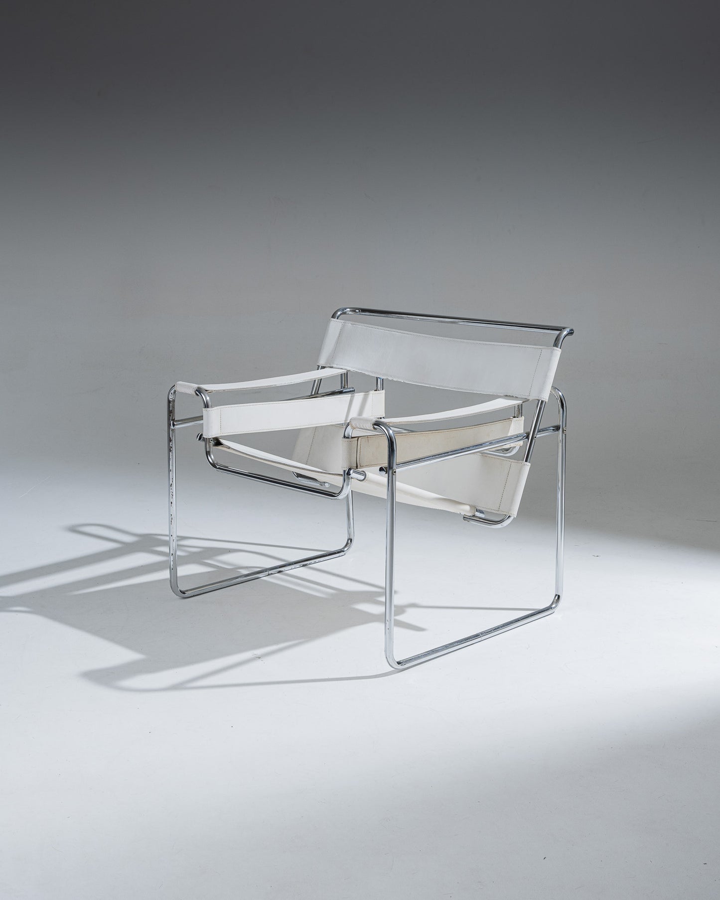 Fauteuil Wassily B3 en cuir Blanc, conçu par Marcel Breuer en 1925 alors qu’il était encore étudiant au Bauhaus, pour l’appartement du peintre Vassily Kandinsky. Cette réédition reprend la structure tubulaire en acier chromé inspirée de l’univers du vélo, et se distingue par ses larges sangles de cuir blanc formant assise, dossier et accoudoirs. Icône du mouvement moderniste, le Wassily est considéré comme le premier fauteuil réalisé en tubes d’acier issus de l’industrie du bâtiment.
État conforme à l'âge, 