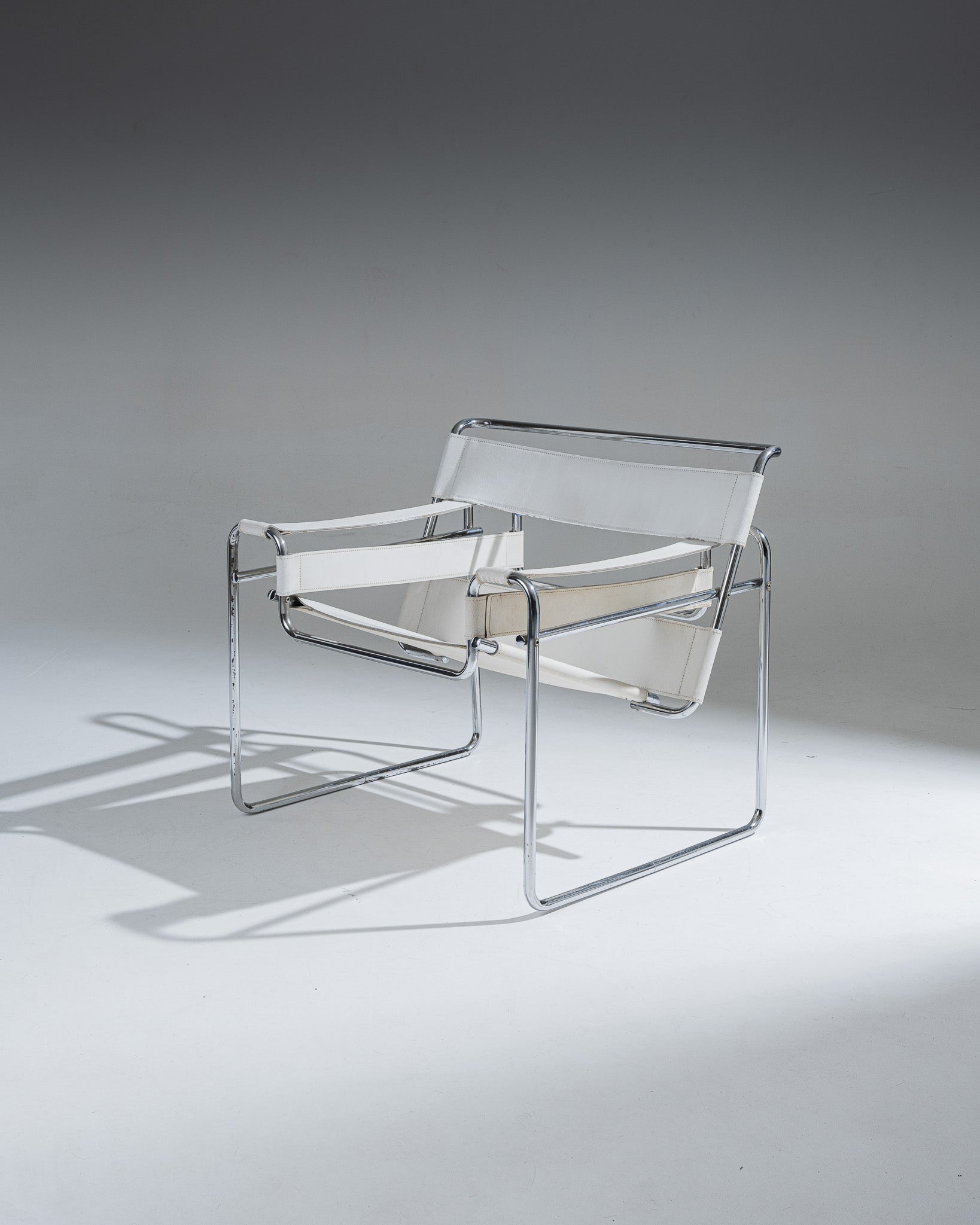 Fauteuil Wassily B3 en cuir Blanc, conçu par Marcel Breuer en 1925 alors qu’il était encore étudiant au Bauhaus, pour l’appartement du peintre Vassily Kandinsky. Cette réédition reprend la structure tubulaire en acier chromé inspirée de l’univers du vélo, et se distingue par ses larges sangles de cuir blanc formant assise, dossier et accoudoirs. Icône du mouvement moderniste, le Wassily est considéré comme le premier fauteuil réalisé en tubes d’acier issus de l’industrie du bâtiment.
État conforme à l'âge, 
