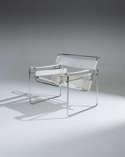 Fauteuil Wassily B3 en cuir Blanc, conçu par Marcel Breuer en 1925 alors qu’il était encore étudiant au Bauhaus, pour l’appartement du peintre Vassily Kandinsky. Cette réédition reprend la structure tubulaire en acier chromé inspirée de l’univers du vélo, et se distingue par ses larges sangles de cuir blanc formant assise, dossier et accoudoirs. Icône du mouvement moderniste, le Wassily est considéré comme le premier fauteuil réalisé en tubes d’acier issus de l’industrie du bâtiment.
État conforme à l'âge, 