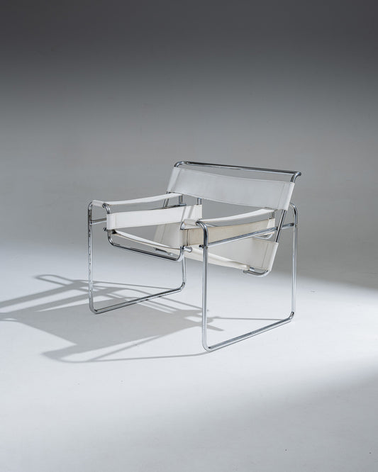 Fauteuil Wassily B3 en cuir Blanc, conçu par Marcel Breuer en 1925 alors qu’il était encore étudiant au Bauhaus, pour l’appartement du peintre Vassily Kandinsky. Cette réédition reprend la structure tubulaire en acier chromé inspirée de l’univers du vélo, et se distingue par ses larges sangles de cuir blanc formant assise, dossier et accoudoirs. Icône du mouvement moderniste, le Wassily est considéré comme le premier fauteuil réalisé en tubes d’acier issus de l’industrie du bâtiment.
État conforme à l'âge, 