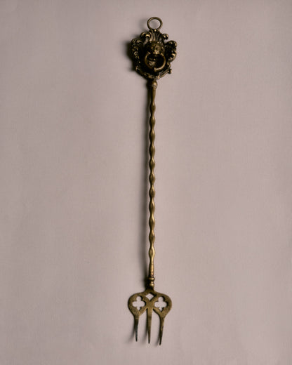Fourche à braise en laiton doré, dotée d'un manche torsadé et d'un trident ajouré à motif de trèfles. La base est ornée d'un mascaron baroque entouré de volutes et de feuillages stylisés.
Bon état général, légère patine conforme à l'âge et à l'usage.