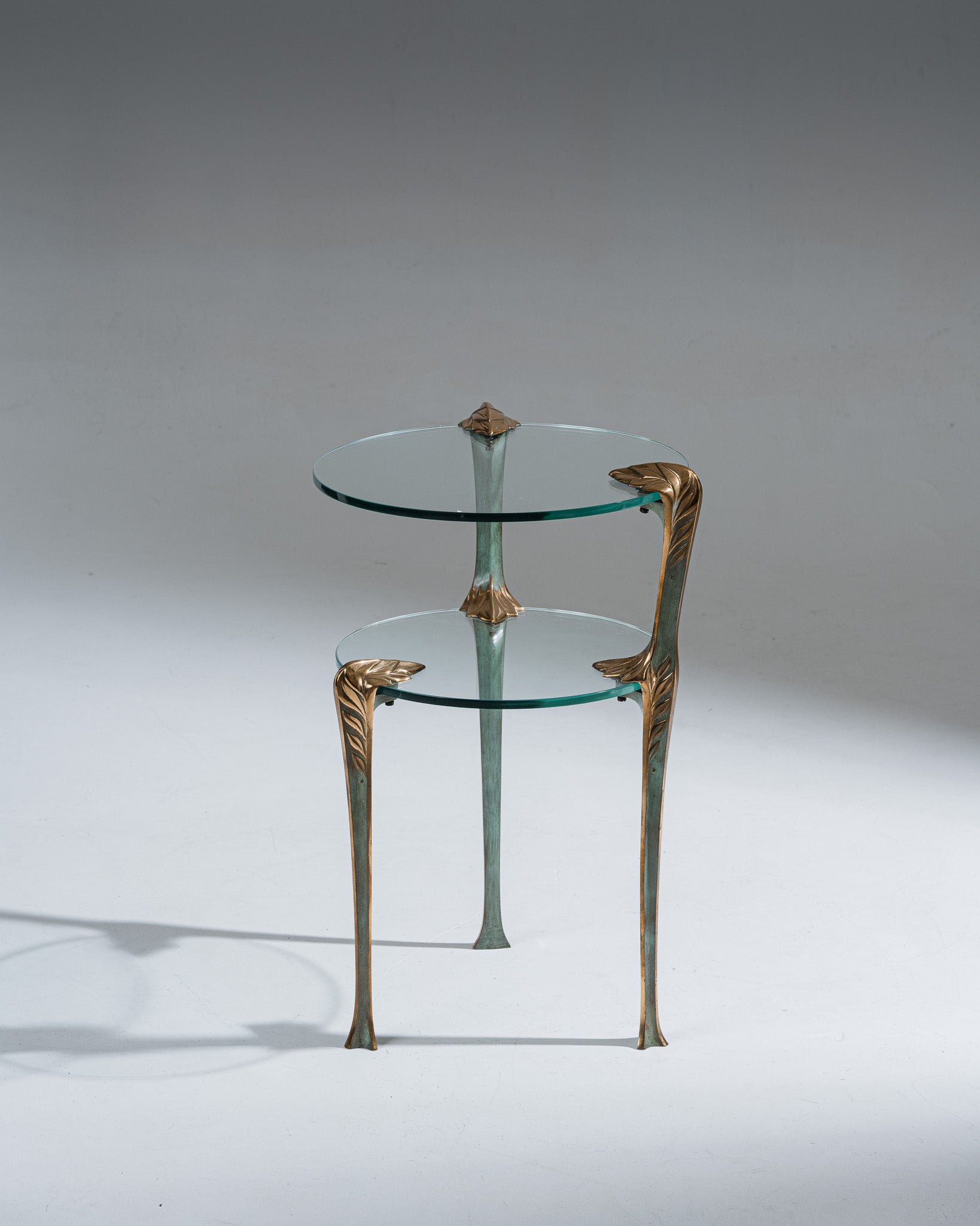 Guéridon tripode en laiton et en verre. Deux plateaux de tailles différentes glissés dans les pieds Décors des montants vert et or en forme de feuilles d'acanthe Art Déco. Se rapprochant des travaux des années 1970. Belle patine.&nbsp;