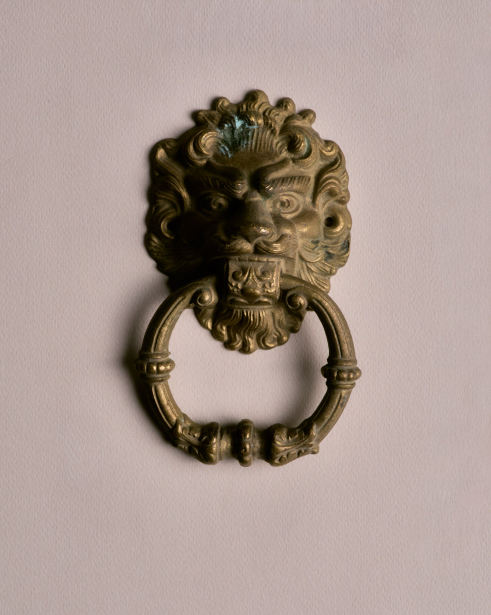 Heurtoir de porte en laiton. Design de tête de lion tenant dans sa gueule un anneau amovible au motif de perles. deux trous dans la crinière pour les fixations. Présente une patine conforme à l'âge et à l'usage ainsi qu'une marque au sommet.&nbsp;