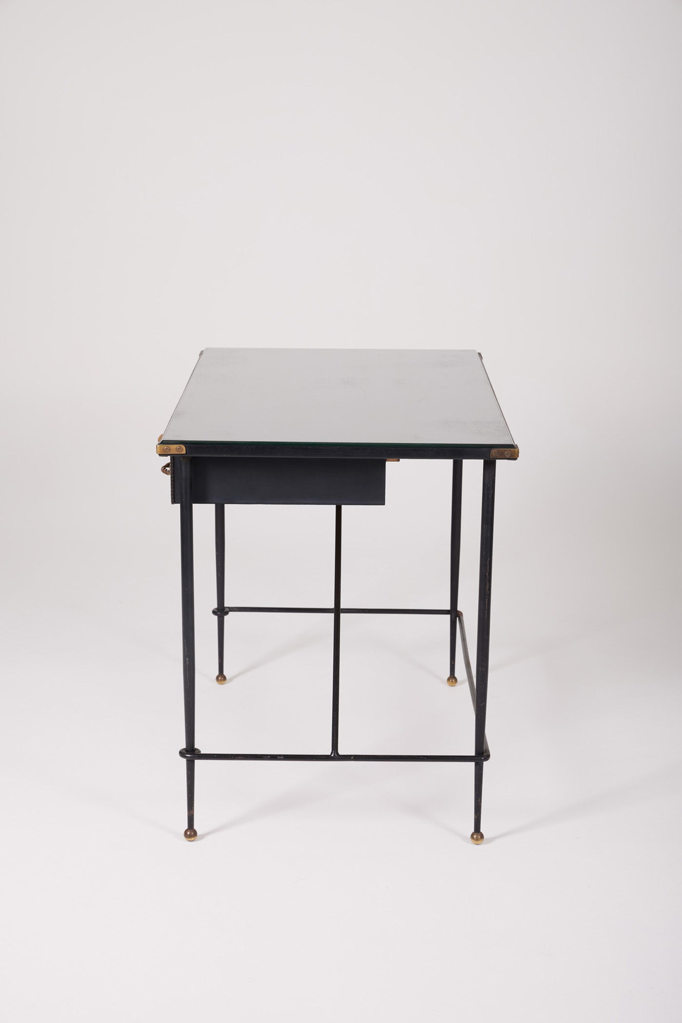  Bureau d'exception du designer Jacques Adnet (1900-1984), années 1940. Le piétement est en fer forgé patiné noir, le plateau en verre et les détails du bureau sont en cuir et laiton. Les deux tiroirs coulissants sont recouverts de cuir piqué à la main. Jacques Adnet a laissé une empreinte indélébile dans le monde du design avec son style distinctif et son innovation constante, il collabora notamment avec la maison Hermès sur des meubles en cuir de haute qualité, sa marque de fabrique.