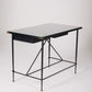  Bureau d'exception du designer Jacques Adnet (1900-1984), années 1940. Le piétement est en fer forgé patiné noir, le plateau en verre et les détails du bureau sont en cuir et laiton. Les deux tiroirs coulissants sont recouverts de cuir piqué à la main. Jacques Adnet a laissé une empreinte indélébile dans le monde du design avec son style distinctif et son innovation constante, il collabora notamment avec la maison Hermès sur des meubles en cuir de haute qualité, sa marque de fabrique.