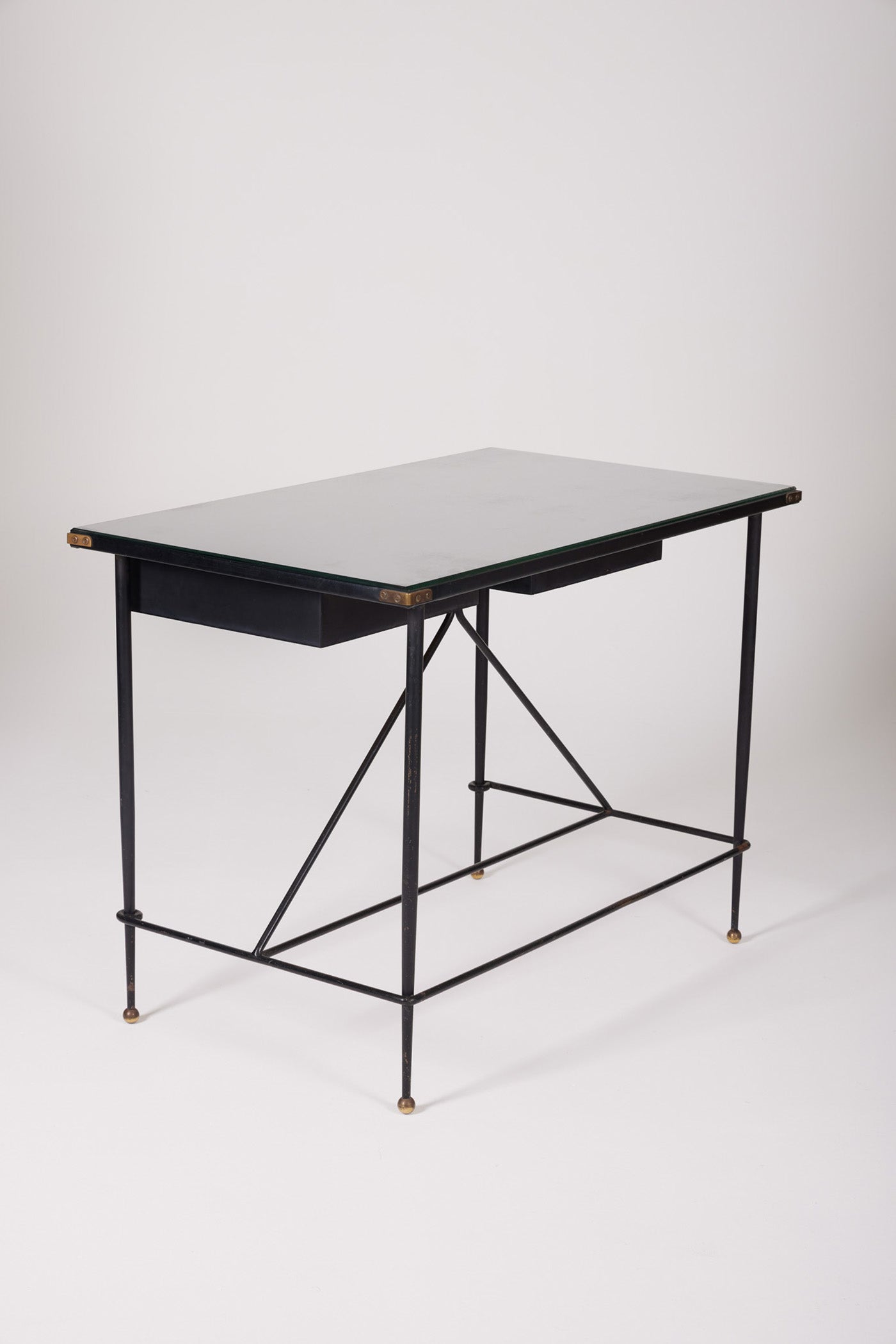  Bureau d'exception du designer Jacques Adnet (1900-1984), années 1940. Le piétement est en fer forgé patiné noir, le plateau en verre et les détails du bureau sont en cuir et laiton. Les deux tiroirs coulissants sont recouverts de cuir piqué à la main. Jacques Adnet a laissé une empreinte indélébile dans le monde du design avec son style distinctif et son innovation constante, il collabora notamment avec la maison Hermès sur des meubles en cuir de haute qualité, sa marque de fabrique.