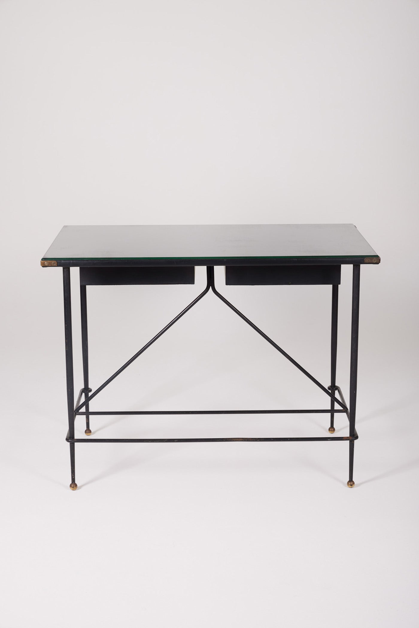  Bureau d'exception du designer Jacques Adnet (1900-1984), années 1940. Le piétement est en fer forgé patiné noir, le plateau en verre et les détails du bureau sont en cuir et laiton. Les deux tiroirs coulissants sont recouverts de cuir piqué à la main. Jacques Adnet a laissé une empreinte indélébile dans le monde du design avec son style distinctif et son innovation constante, il collabora notamment avec la maison Hermès sur des meubles en cuir de haute qualité, sa marque de fabrique.