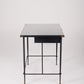  Bureau d'exception du designer Jacques Adnet (1900-1984), années 1940. Le piétement est en fer forgé patiné noir, le plateau en verre et les détails du bureau sont en cuir et laiton. Les deux tiroirs coulissants sont recouverts de cuir piqué à la main. Jacques Adnet a laissé une empreinte indélébile dans le monde du design avec son style distinctif et son innovation constante, il collabora notamment avec la maison Hermès sur des meubles en cuir de haute qualité, sa marque de fabrique.