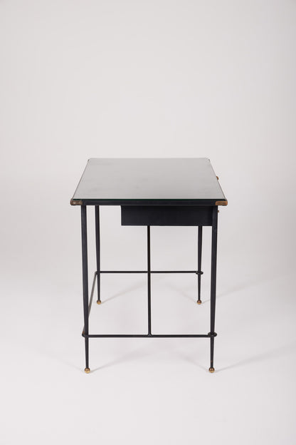  Bureau d'exception du designer Jacques Adnet (1900-1984), années 1940. Le piétement est en fer forgé patiné noir, le plateau en verre et les détails du bureau sont en cuir et laiton. Les deux tiroirs coulissants sont recouverts de cuir piqué à la main. Jacques Adnet a laissé une empreinte indélébile dans le monde du design avec son style distinctif et son innovation constante, il collabora notamment avec la maison Hermès sur des meubles en cuir de haute qualité, sa marque de fabrique.