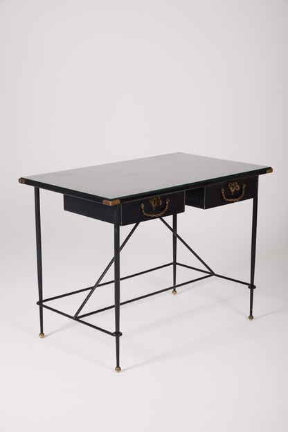  Bureau d'exception du designer Jacques Adnet (1900-1984), années 1940. Le piétement est en fer forgé patiné noir, le plateau en verre et les détails du bureau sont en cuir et laiton. Les deux tiroirs coulissants sont recouverts de cuir piqué à la main. Jacques Adnet a laissé une empreinte indélébile dans le monde du design avec son style distinctif et son innovation constante, il collabora notamment avec la maison Hermès sur des meubles en cuir de haute qualité, sa marque de fabrique.