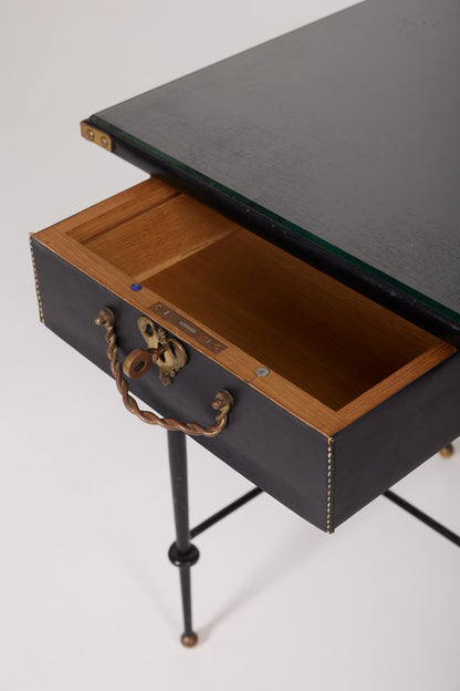  Bureau d'exception du designer Jacques Adnet (1900-1984), années 1940. Le piétement est en fer forgé patiné noir, le plateau en verre et les détails du bureau sont en cuir et laiton. Les deux tiroirs coulissants sont recouverts de cuir piqué à la main. Jacques Adnet a laissé une empreinte indélébile dans le monde du design avec son style distinctif et son innovation constante, il collabora notamment avec la maison Hermès sur des meubles en cuir de haute qualité, sa marque de fabrique.