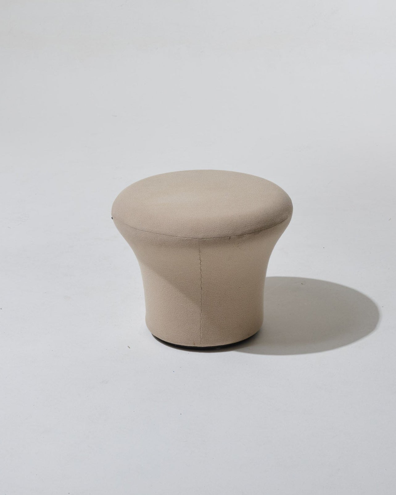 Fauteuil Mushroom de Pierre Paulin, années 1970. Dans une esthétique typique du Space Age, il se compose d'une coque en fibre de verre, garni de son tissu Kvadrat beige. Le pied circulaire évasé forme d’un seul tenant l’assise et le dossier, également circulaires. Le tissu présente une usure, cohérente avec l’âge et l’usage.