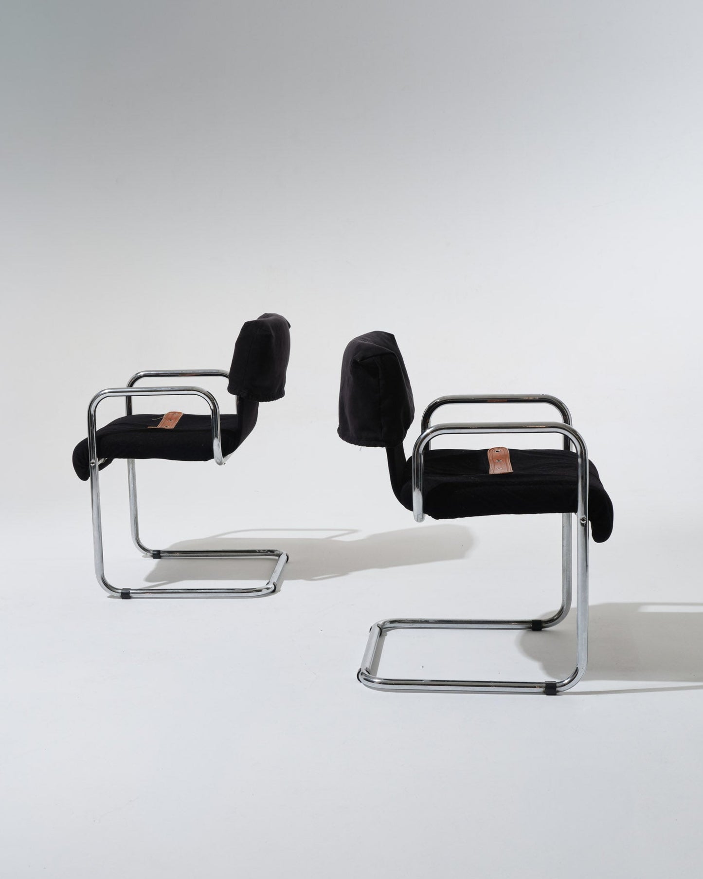 Paire de chaises de Guido Faleschini pour Mariani dans les années 1970. Structure en acier tubulaire chromé, assise et dossier généreusement rembourrés et recouverts d'un velours noir profond. Une sangle en cuir cognac, fixée par oeillets métalliques, souligne la ligne du siège.