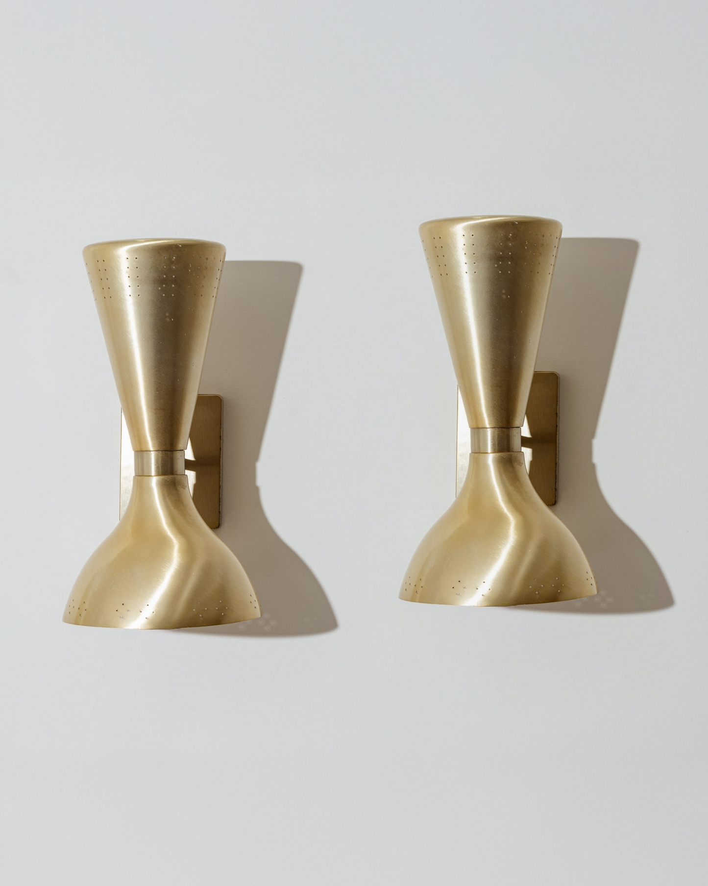 Paire d’appliques murales en laiton brossé, dites “Diabolo”, typiques du design italien des années 1960. Chaque applique présente un double abat-jour orientable, perforé sur les bords pour diffuser une lumière douce et ponctuelle. Très bel état.