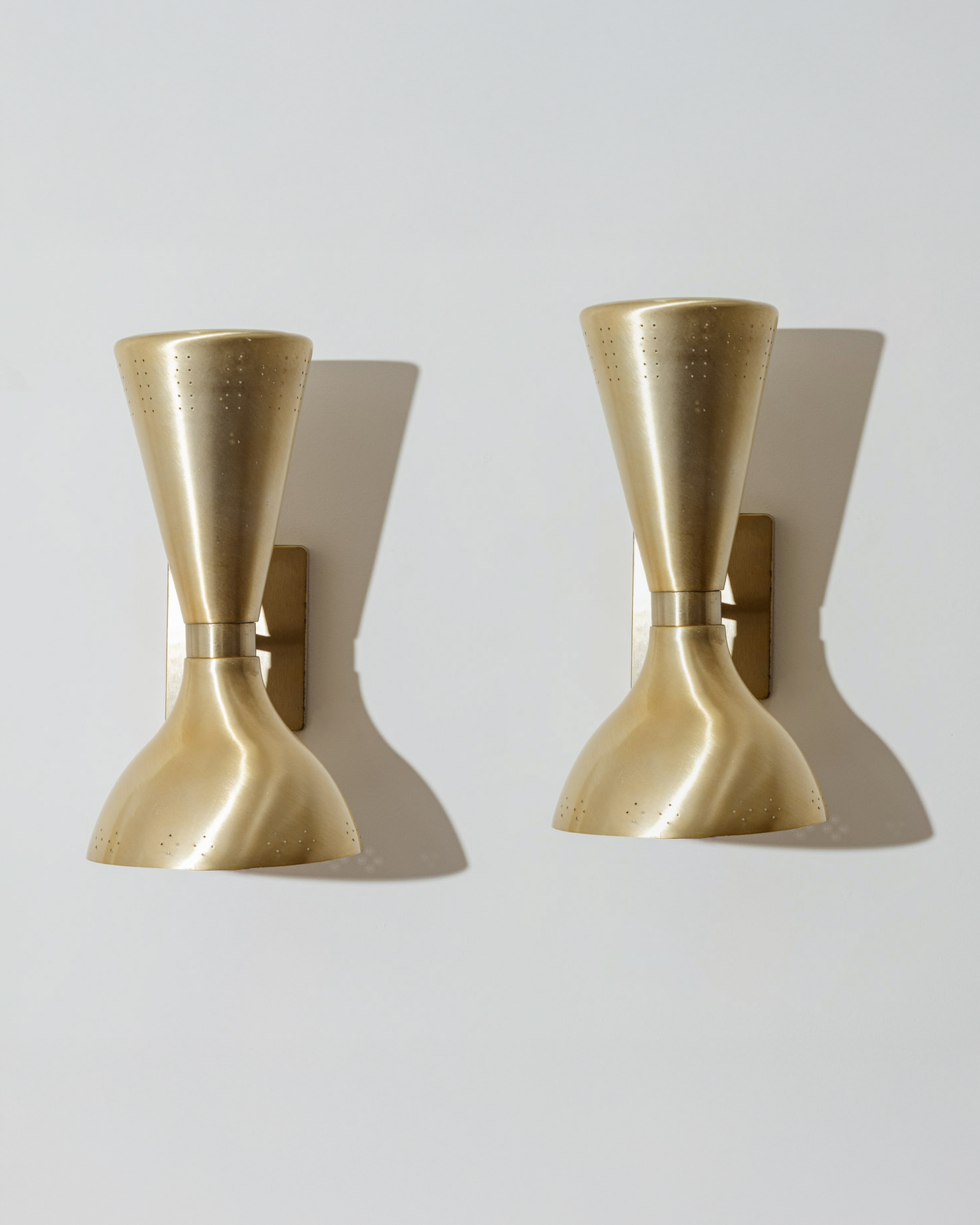 Paire d’appliques murales en laiton brossé, dites “Diabolo”, typiques du design italien des années 1960. Chaque applique présente un double abat-jour orientable, perforé sur les bords pour diffuser une lumière douce et ponctuelle. Très bel état.
