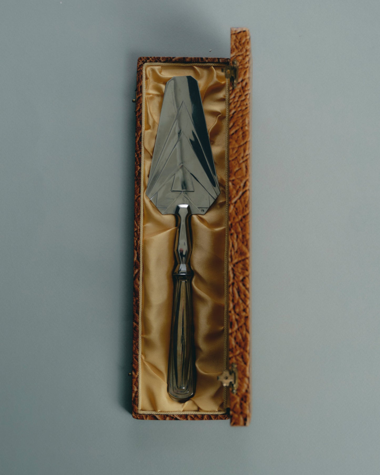 Pelle de service en métal argenté, à décor géométrique typique de la période Art Déco. Manche facetté orné de reliefs symétriques, lame triangulaire finement ciselée. Présentée dans son coffret gainé d'origine. Travail européen, circa 1930-40.

Très bel état général, légère patine conforme à l'âge.