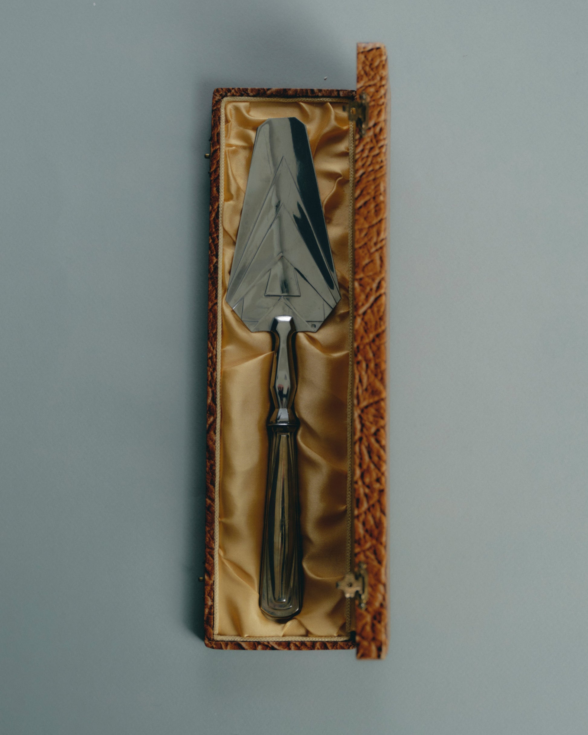 Pelle de service en métal argenté, à décor géométrique typique de la période Art Déco. Manche facetté orné de reliefs symétriques, lame triangulaire finement ciselée. Présentée dans son coffret gainé d'origine. Travail européen, circa 1930-40.

Très bel état général, légère patine conforme à l'âge.
