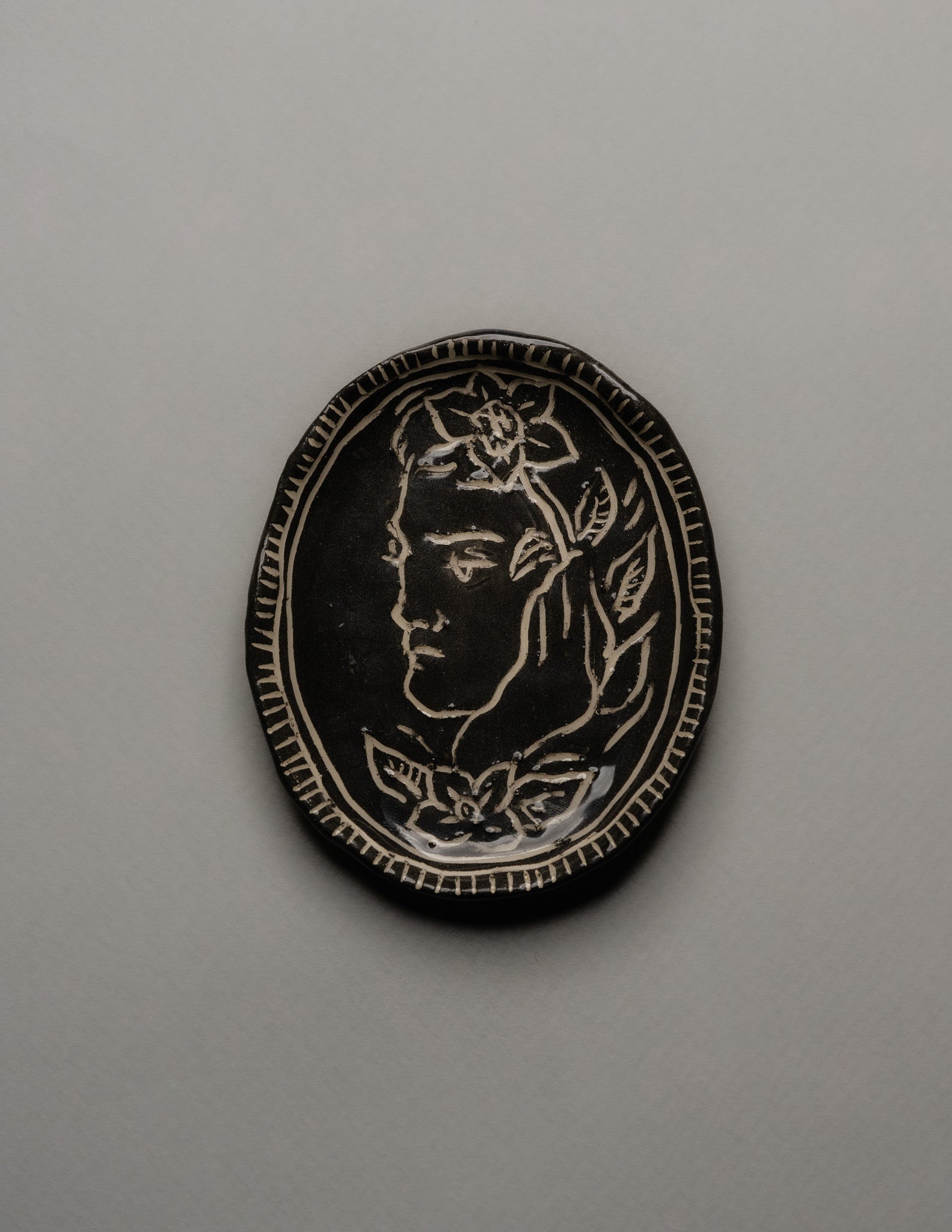 Petit vide-poche ovale en céramique émaillée noire, décor gravé d'un profil masculin orné de fleurs. Bordure finement striée à la main. Signature en creux ELDAROV. T au revers. Parfait état.