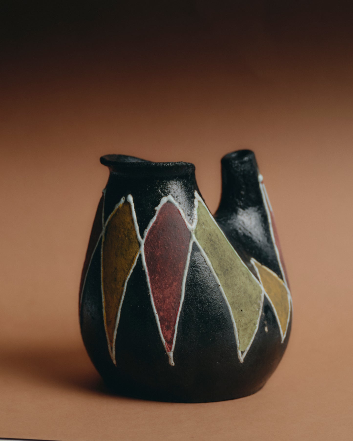 Pichet en grès texturé signé Atelier Accolay, circa 1950-60. Corps galbé à double ouverture, décor en relief aux motifs géométriques dans des tons ocre, vert olive et brun rouge sur fond noir mat. En superbe état.