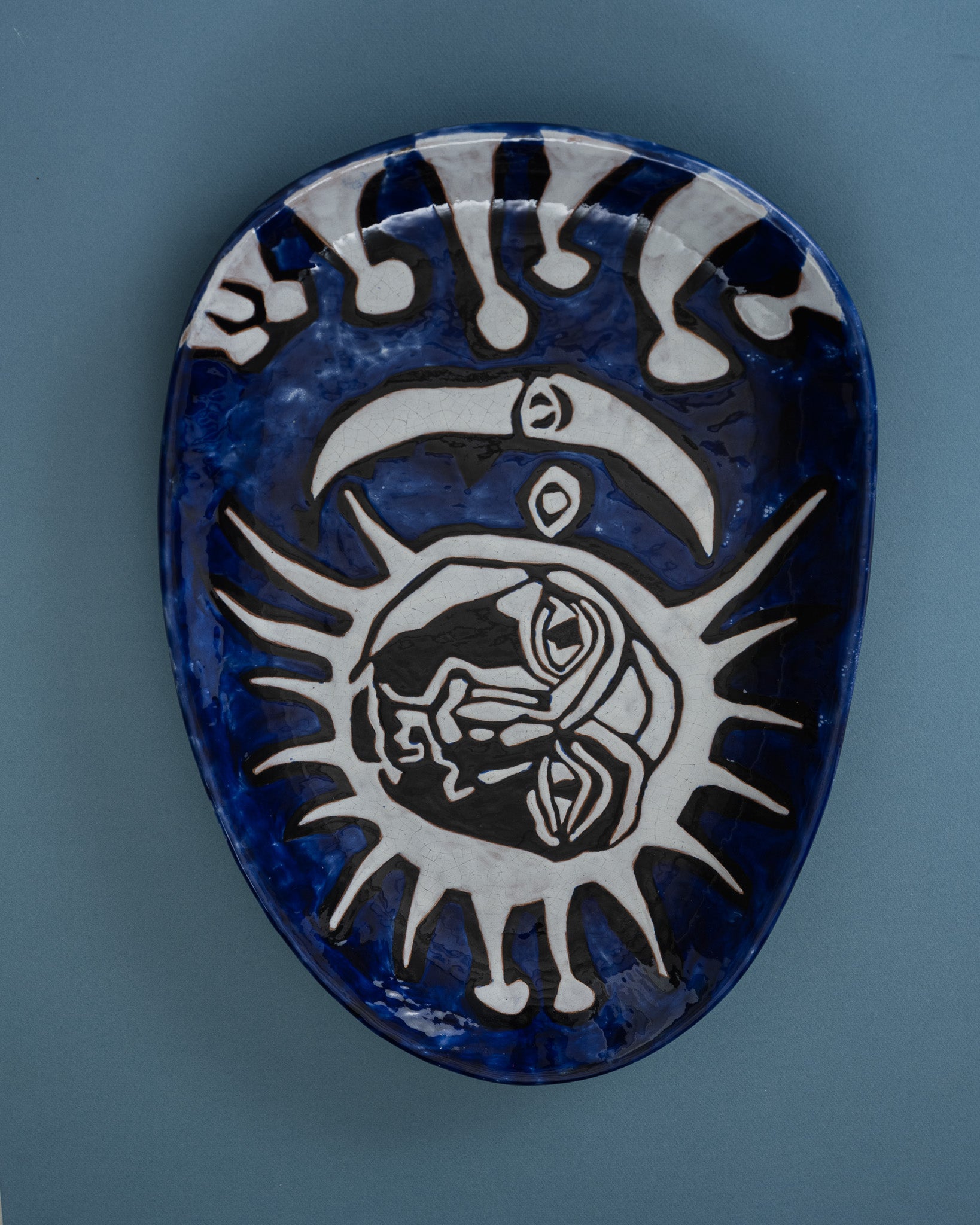 Plat en céramique émaillé, signé Jean Lurçat (1892-1966) pour l'atelier Sant-Vicens, réalisé dans les années 1950. Décor central représentant un soleil et une lune stylisés, motif emblématique de l'imaginaire cosmique de Lurçat : visages graphiques et lignes gravées noires. Émail bleu profond caractéristique de Sant-Vicens, contrasté par un fond blanc-créme rehaussé de contours gravés sombres.&nbsp;
Pièce numérotée 49/50, portant la signature manuscrite&nbsp;"J. Lurçat - Saint-Vicens". Parfait état.