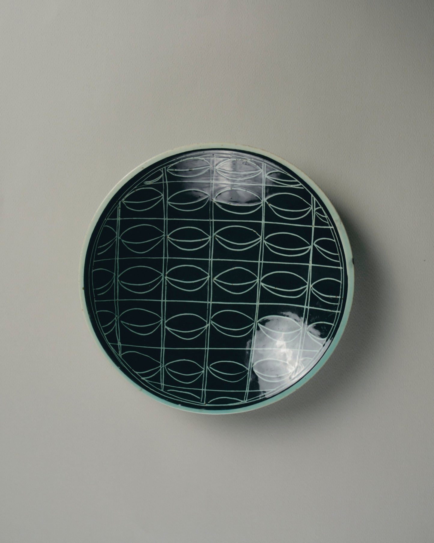 Plat rond en céramique émaillée, attribué à Jacques Pouchain (Atelier Dieulefit), vers 1970. Décor géométrique incisé à motifs linéaires entrecroisés, émaillé noir et vert d'eau sur fond clair. Bel état général, à noter de légères marques d'usage sur le bord.