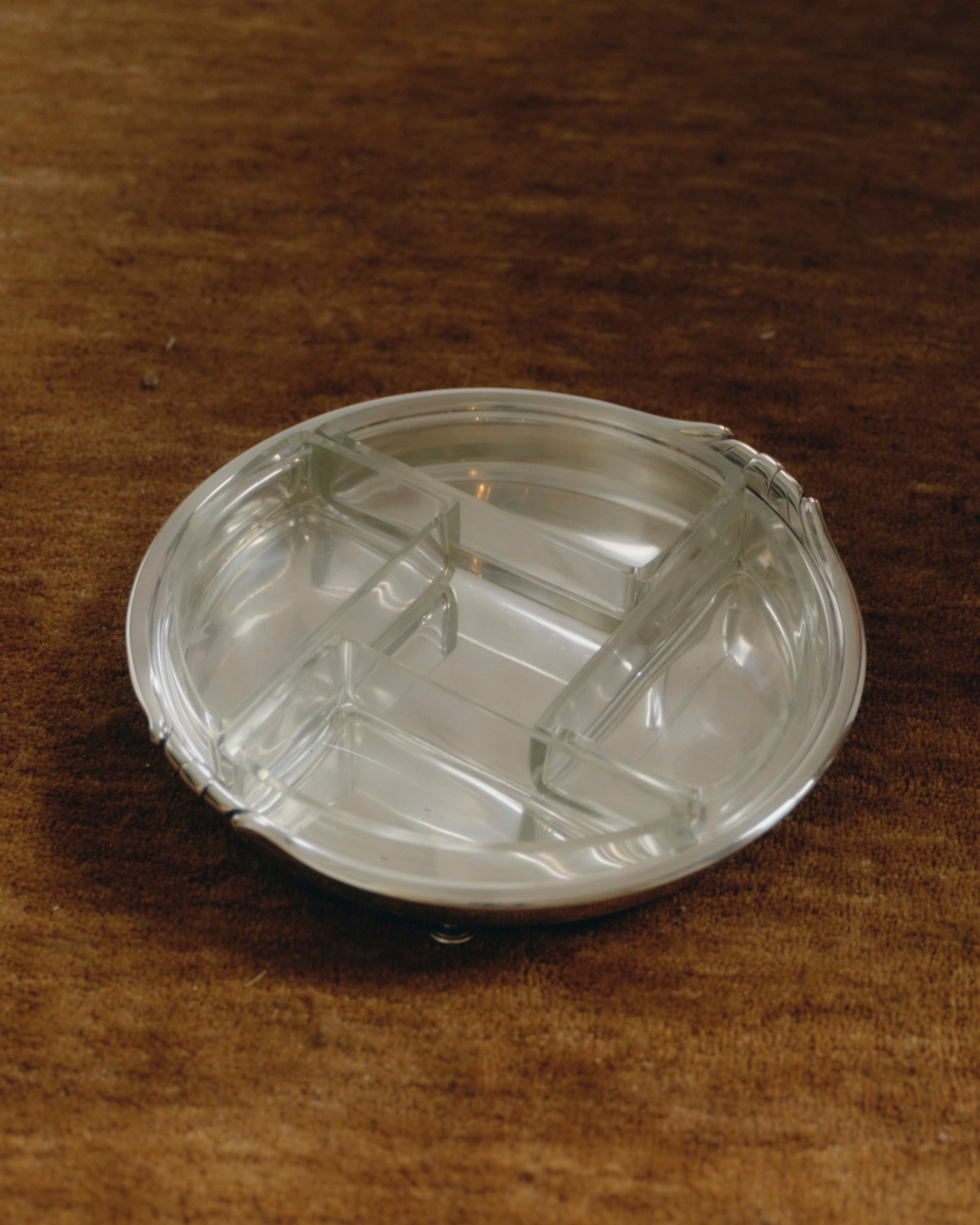 Plat circulaire à quatre compartiments amovibles en verre moulé, reposant sur une base en métal argenté à trois pieds boules. Lignes épurées et géométrie équilibrée caractéristiques du style Art Déco. Travail européen des années 1930.
Bel état vintage, légère patine conforme à l'âge.