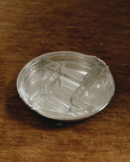 Plat circulaire à quatre compartiments amovibles en verre moulé, reposant sur une base en métal argenté à trois pieds boules. Lignes épurées et géométrie équilibrée caractéristiques du style Art Déco. Travail européen des années 1930.
Bel état vintage, légère patine conforme à l'âge.