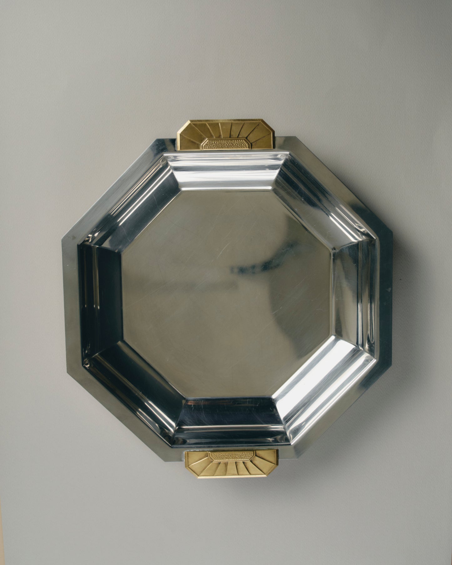 Plat octogonal en acier inoxydable 18/10 à anses en laiton doré, signé Jean Couzon pour Charleston France, vers 1970s. Modèle typique du style Art Déco, reconnaissable à ses lignes géométriques précises et à ses poignées en laiton mouluré à décor symétrique.
Bon été général, présentant de légères traces d'usage conformes à l'âge. Signature gravée sous la base.