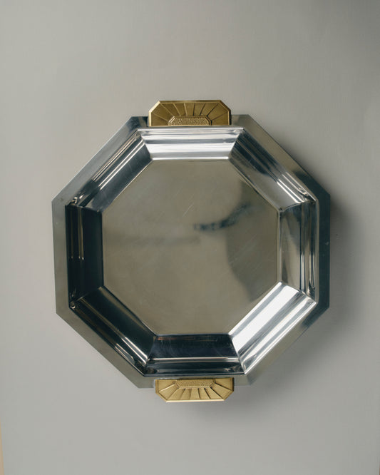 Plat octogonal en acier inoxydable 18/10 à anses en laiton doré, signé Jean Couzon pour Charleston France, vers 1970s. Modèle typique du style Art Déco, reconnaissable à ses lignes géométriques précises et à ses poignées en laiton mouluré à décor symétrique.
Bon été général, présentant de légères traces d'usage conformes à l'âge. Signature gravée sous la base.