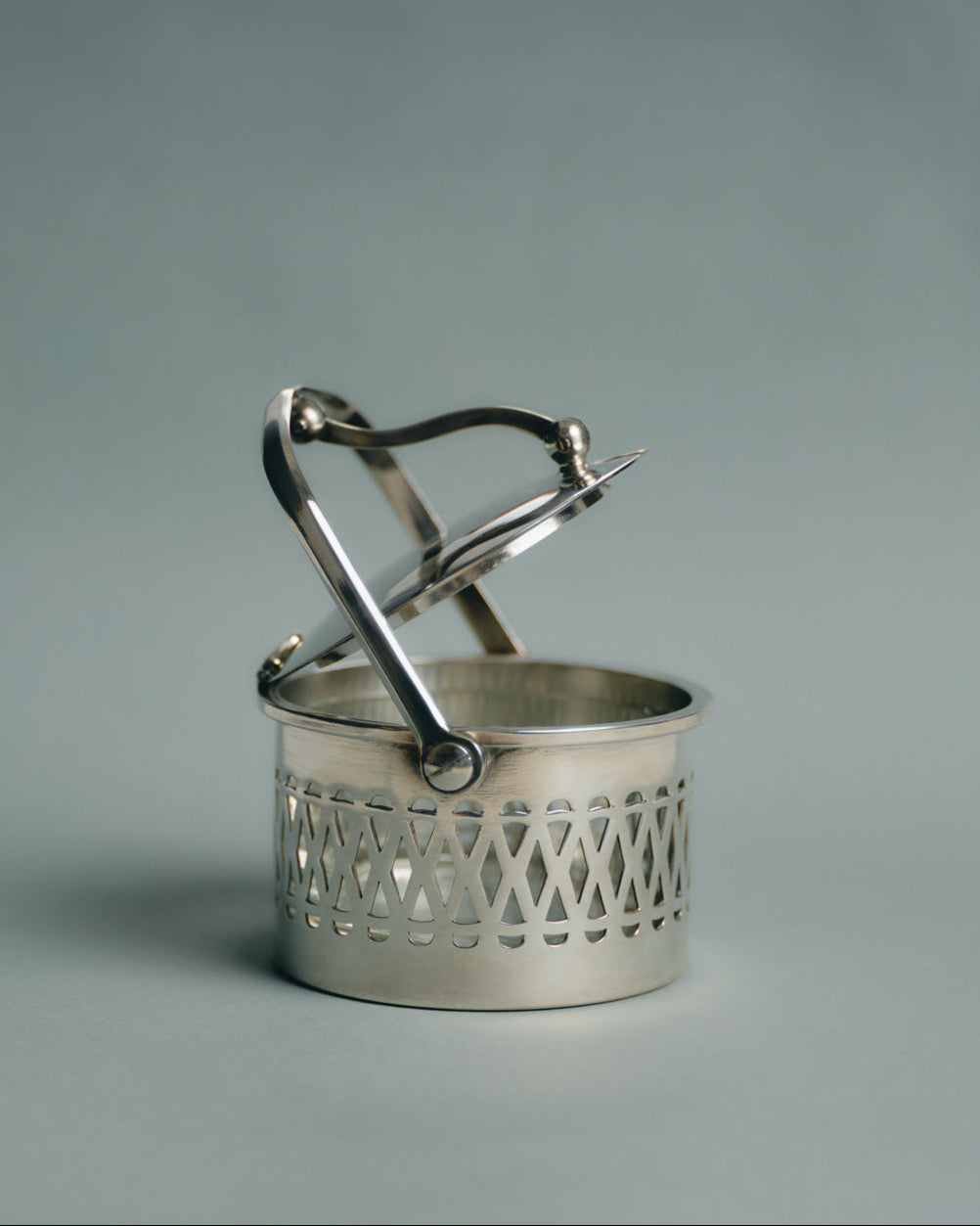 Pot de service à parmesan ou confiture en métal argenté et verre, travail français des années 1950. Monture ajourée à motif de croisillons, couvercle assorti et anse latérale fine. Le récipient intérieur est en verre épais transparent — également appelé verre-confiturier. Anse latérale fine et couvercle assorti.
Très bon état général, légères traces d’usage conformes à l’âge.