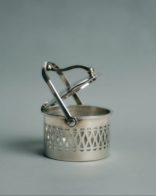 Pot de service à parmesan ou confiture en métal argenté et verre, travail français des années 1950. Monture ajourée à motif de croisillons, couvercle assorti et anse latérale fine. Le récipient intérieur est en verre épais transparent — également appelé verre-confiturier. Anse latérale fine et couvercle assorti.
Très bon état général, légères traces d’usage conformes à l’âge.