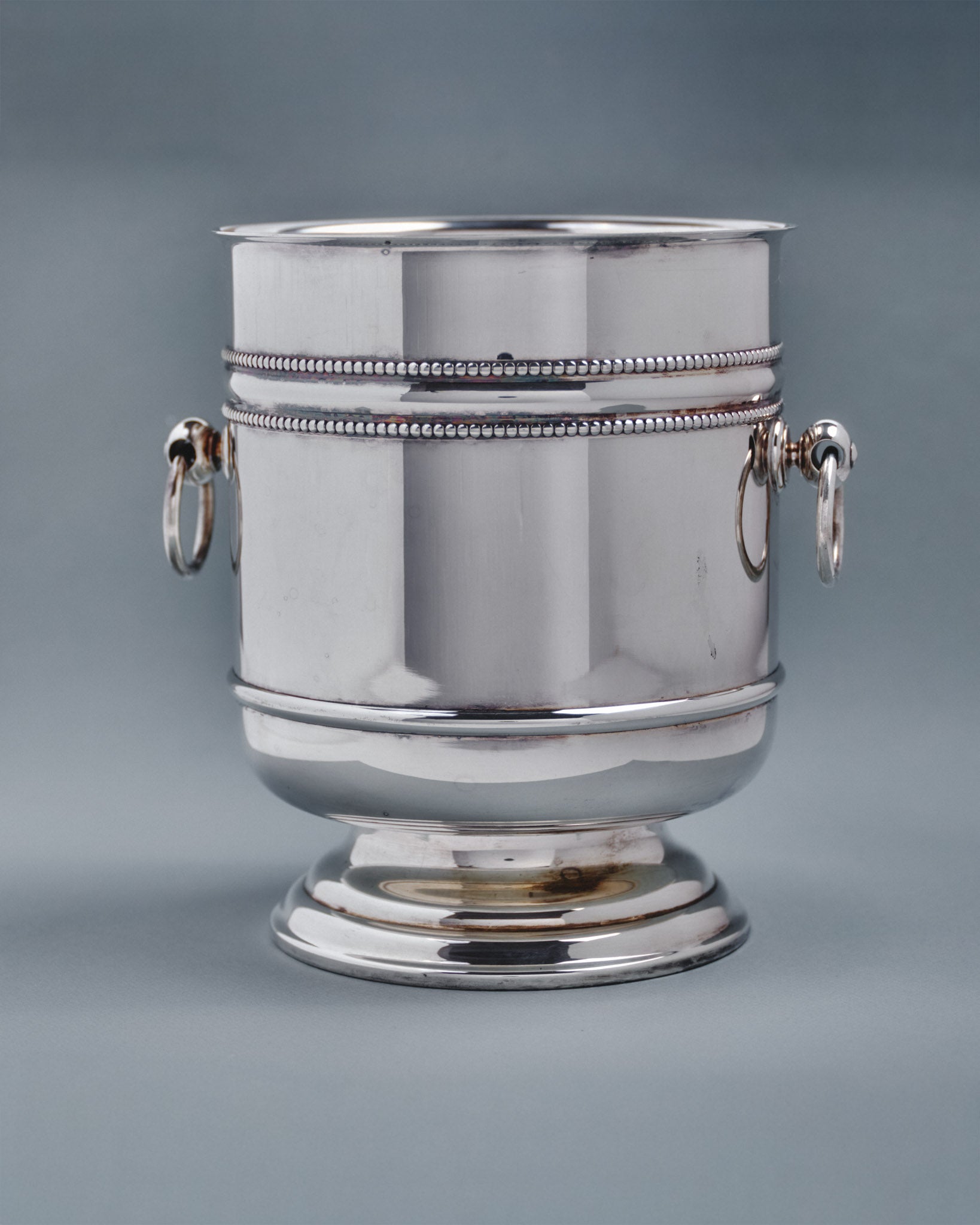 Seau à champagne de la maison Christofle, modèle "Perles" en métal argenté. De forme tulipe sur piédouche à décor de frises de perles et prises à anneaux mobiles. Signé et poinçon de maître.