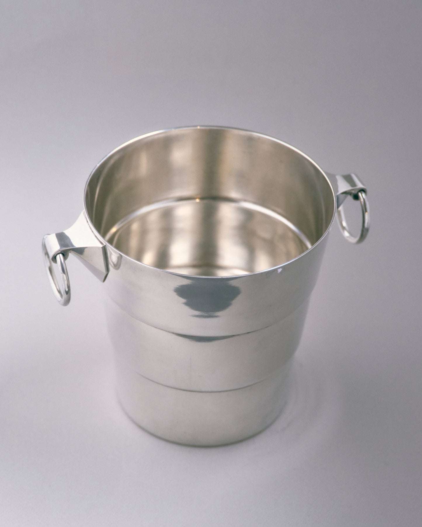 Seau à champagne en métal argenté à décor de bandes horizontales, muni de deux anses à anneaux fixées sur attaches géométriques. Travail des années 1930. Poinçonné sous la base.

Très bon état général, légère patine conforme à l'âge.