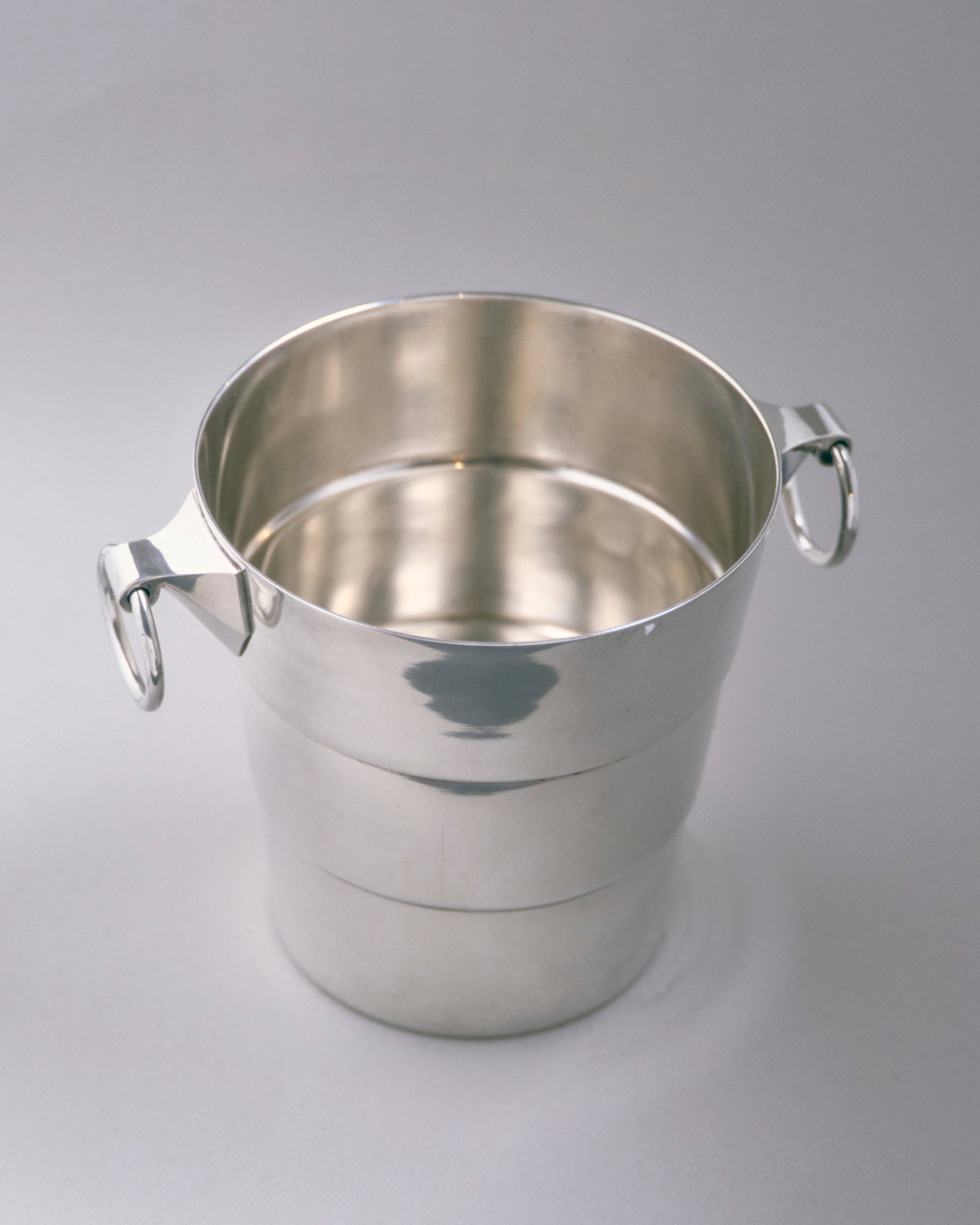 Seau à champagne en métal argenté à décor de bandes horizontales, muni de deux anses à anneaux fixées sur attaches géométriques. Travail des années 1930. Poinçonné sous la base.

Très bon état général, légère patine conforme à l'âge.